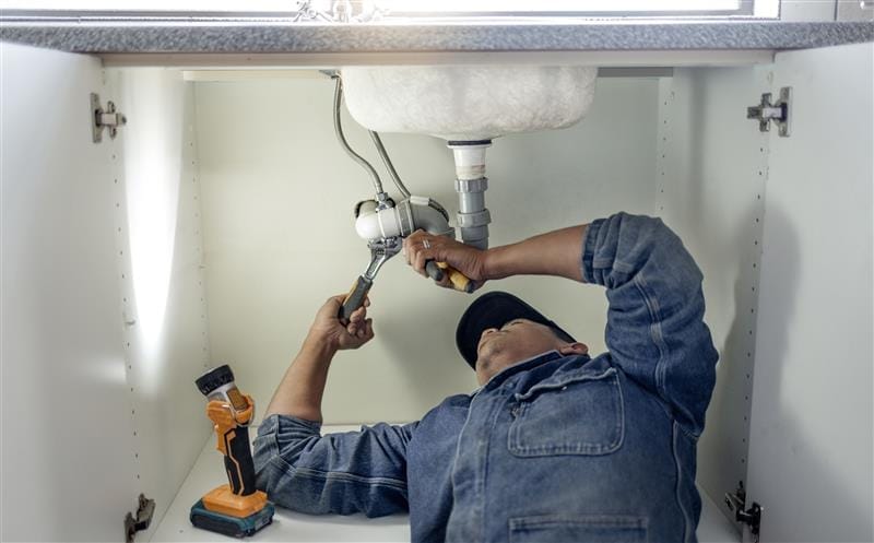 Plumber repairing pipes beneath a bathroom sink in West Valley City