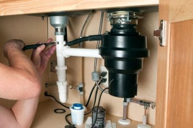 Plumber repairing a garbage disposal beneath a kitchen sink in West Valley City