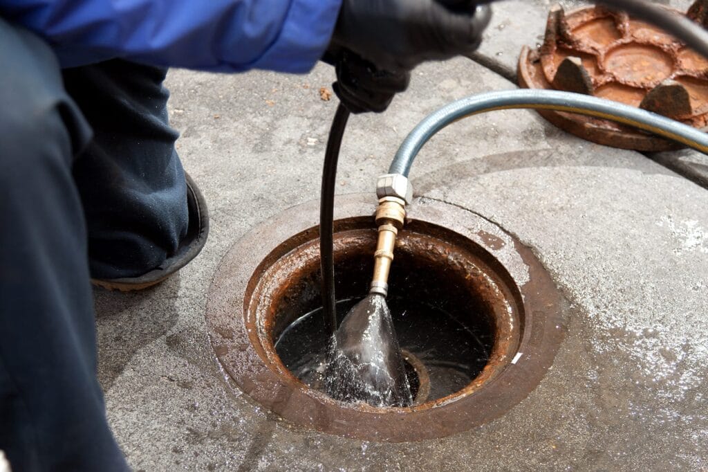 Plumber hydro jetting a sewer line through a manhole in West Valley City