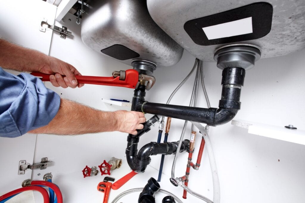 Plumber repairing drain pipes beneath a kitchen sink in West Valley City